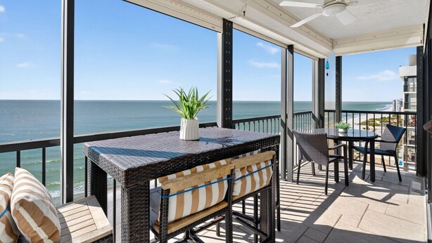 Un balcon avec vue sur l’océan, une table avec des chaises et un ventilateur de plafond.