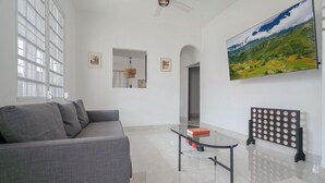 A modern living room with a grey sofa, a glass coffee table, and a large landscape painting on the wall.