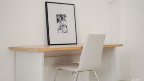 A minimalist workspace with a wooden desk, a white chair, and a framed picture on the wall.