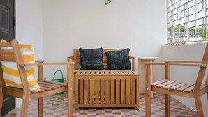 A wooden bench with two black cushions, a green wall decoration, and a window with a grid pattern.