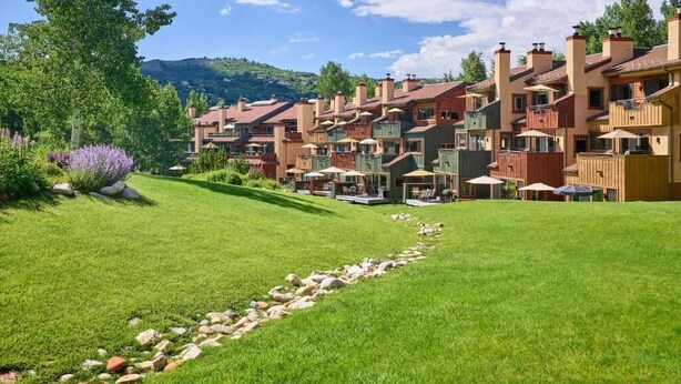 A row of multi-story buildings with balconies, a well-maintained lawn, and a clear sky. - Gorgeous View, 3 minute shuttle  to ski lifts Renovated- Great Location  (Snowmass Village)