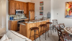 A kitchen with wooden cabinets, a granite countertop, and a bar area with stools. - Gorgeous View, 3 minute shuttle  to ski lifts Renovated- Great Location  (Snowmass Village)