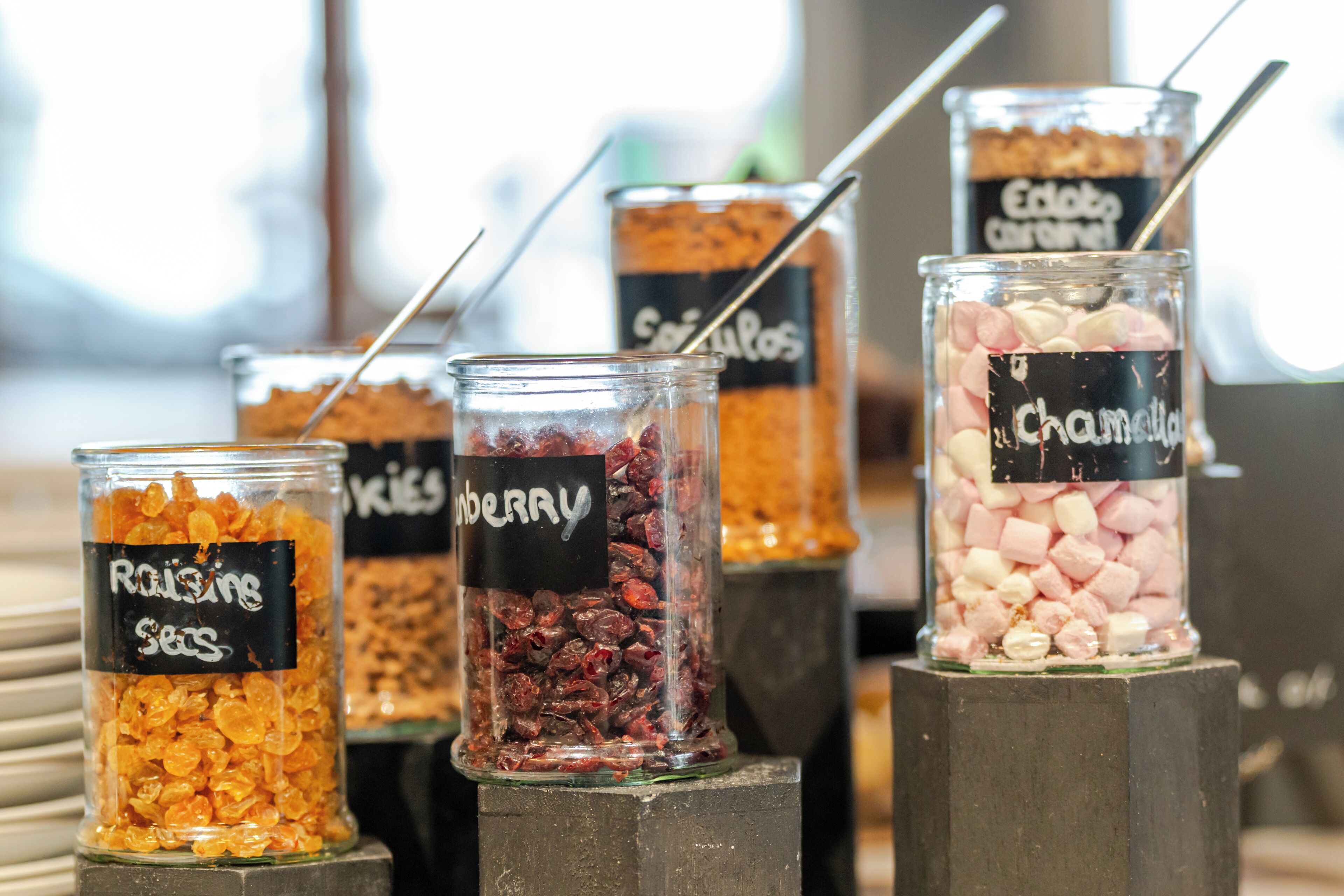 A display of various dried fruits in glass jars with labels, including raisins, cranberries, and cherries.