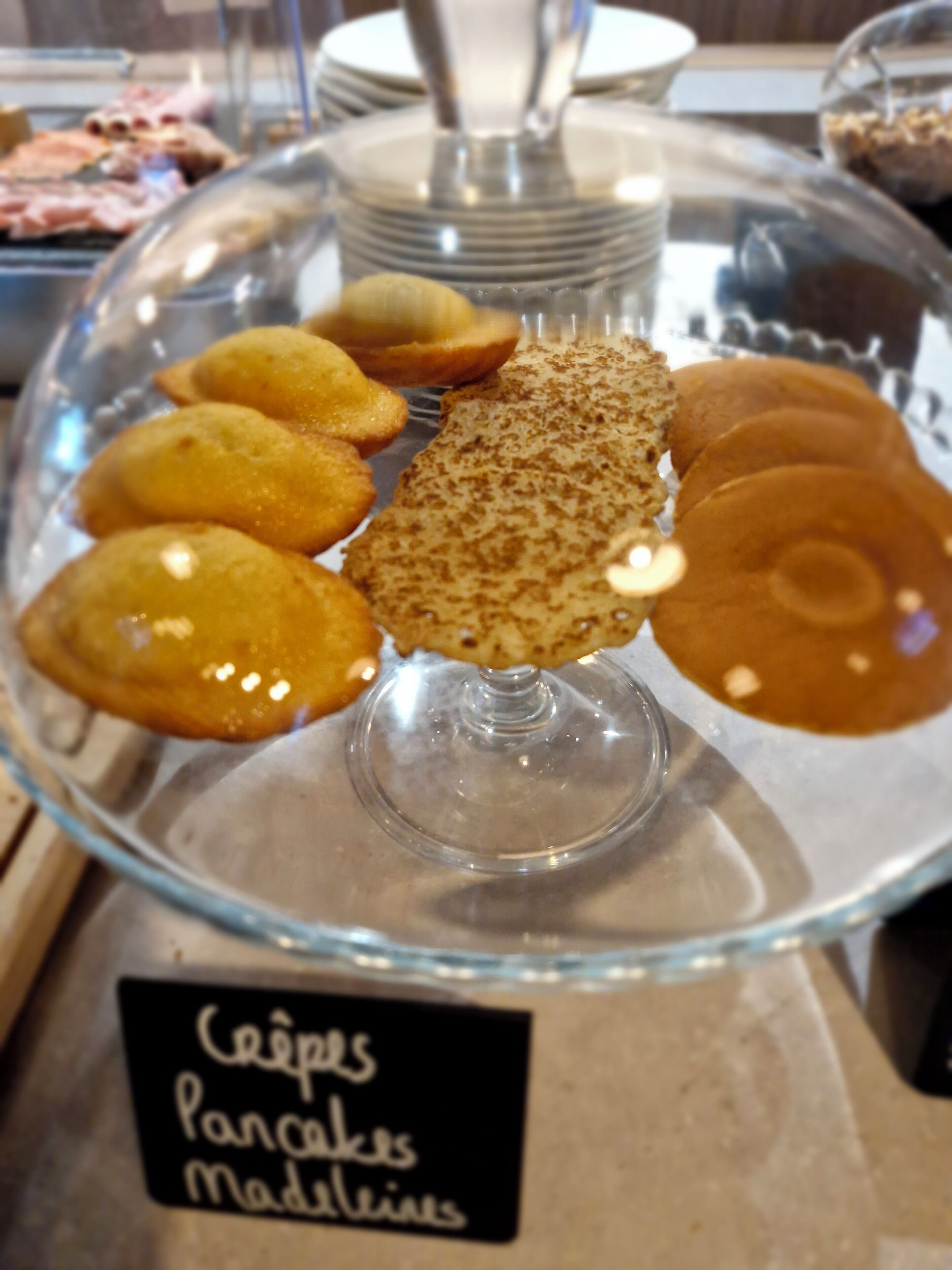 Un expositor de vidrio con varios pasteles, incluyendo crepes y tortitas.