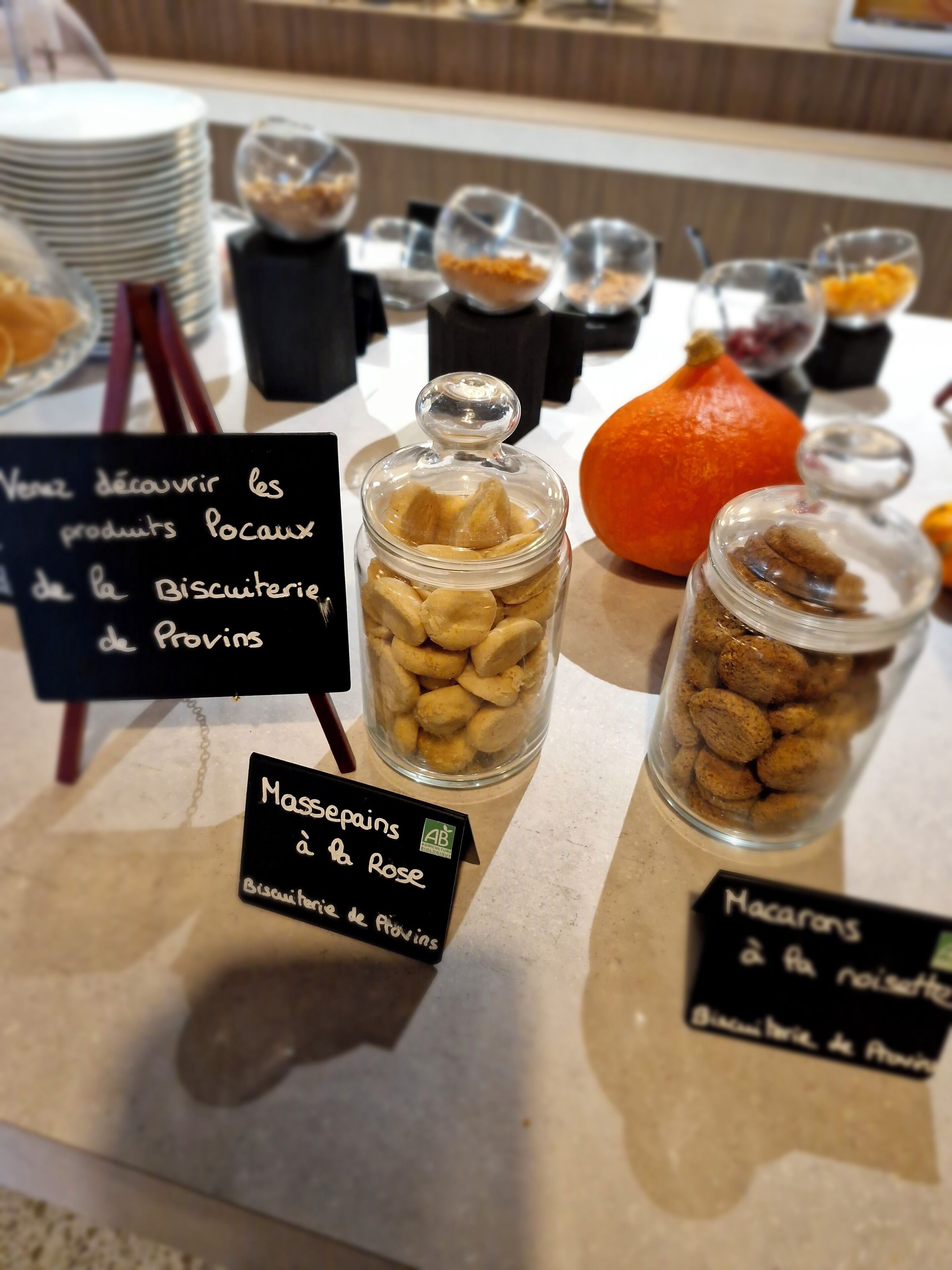 Een buffettafel met diverse etenswaren, waaronder potjes met macarons en amandelhoen, en een bordje dat aangeeft dat de bakkerij uit Provins komt.