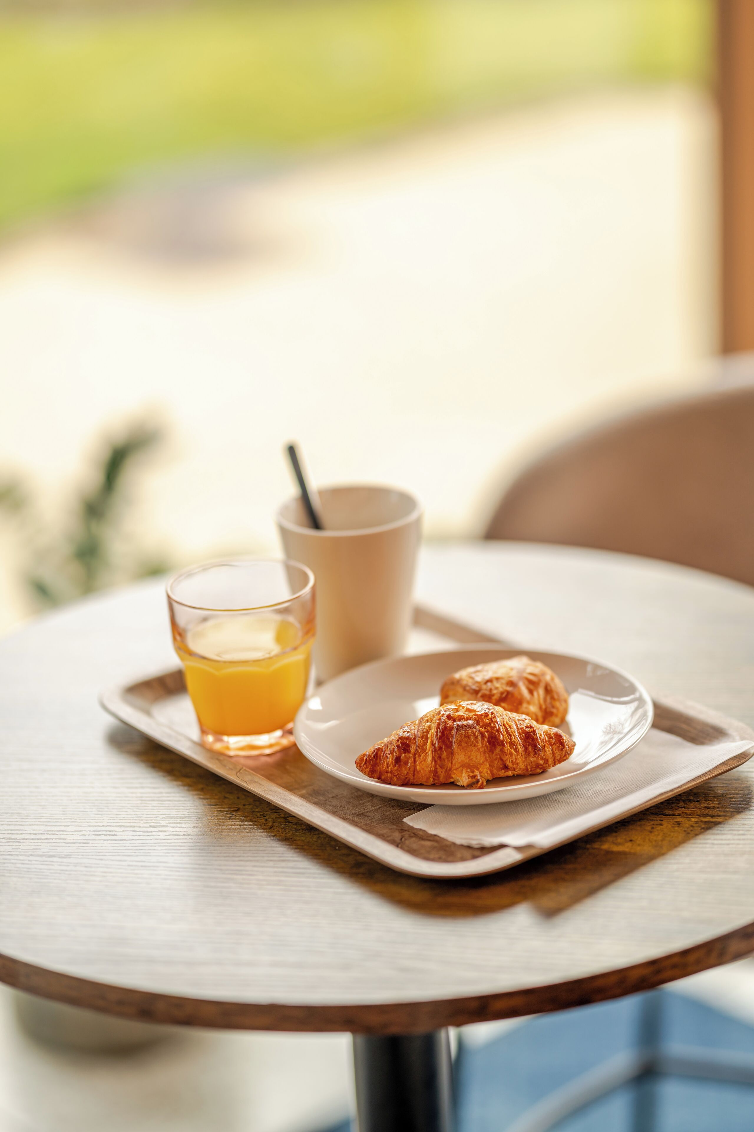 A breakfast tray with croissants and a glass of orange juice on a wooden table.