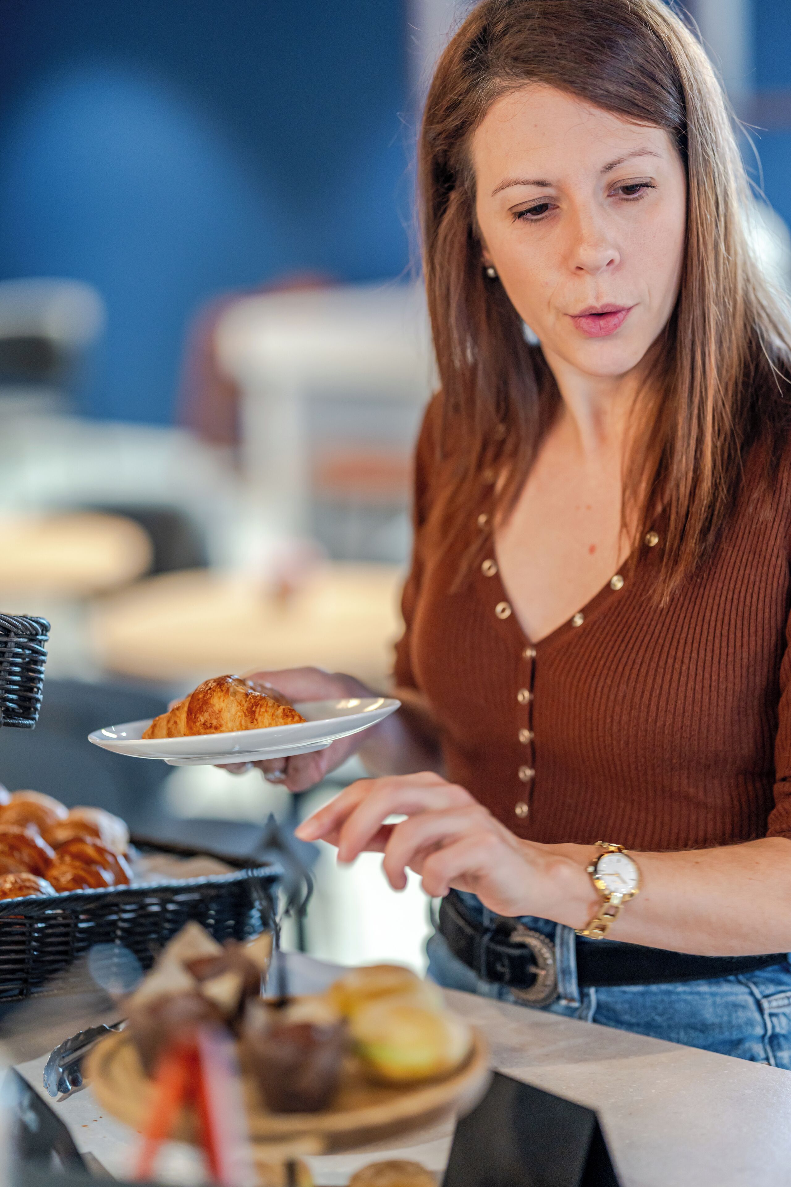 Een vrouw serveert eten bij een buffet met diverse gerechten en een broodmand.