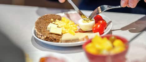 Une personne est en train de prendre un repas, avec une assiette devant elle contenant des œufs, des tomates et une tranche de pain.