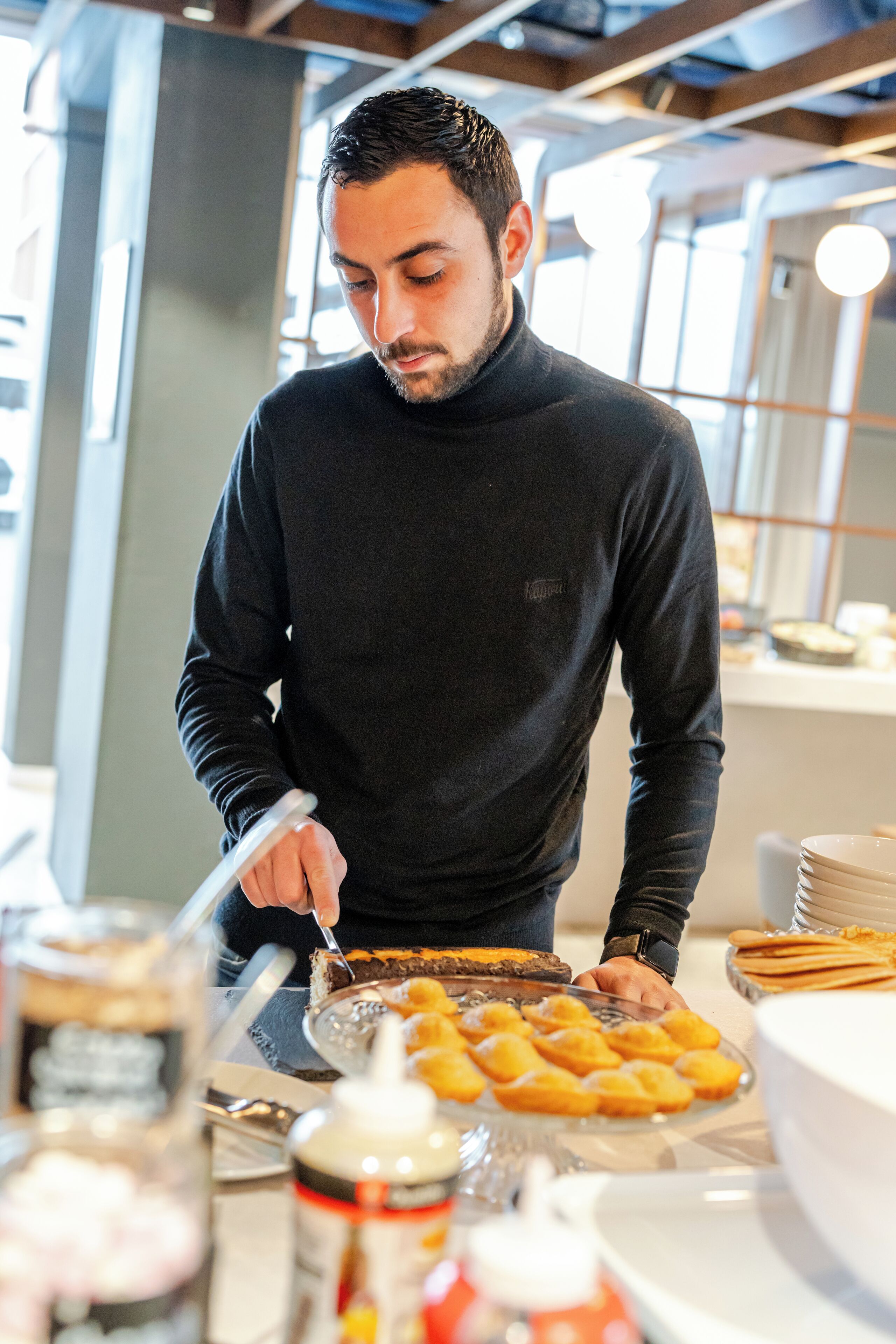 A person serving food at a buffet with various dishes and condiments.