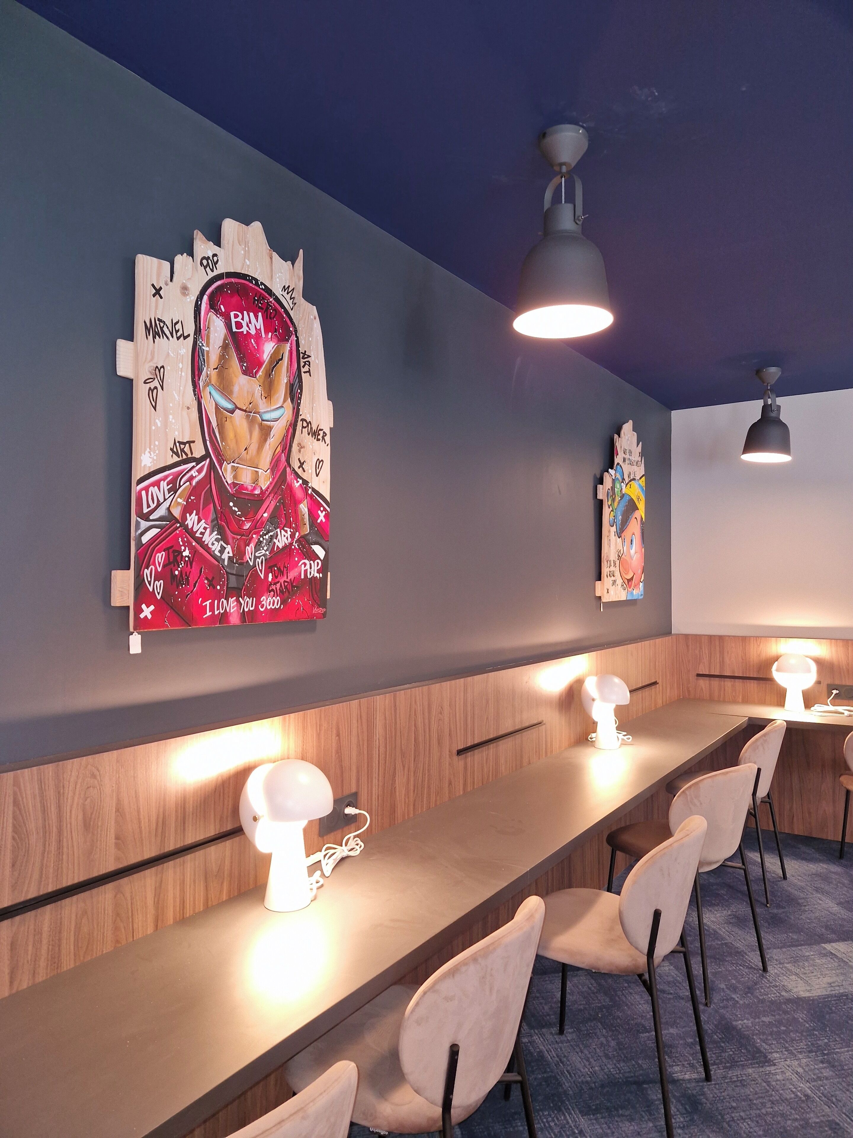 A modern bar area with a long counter, several chairs, and wall art featuring a superhero.