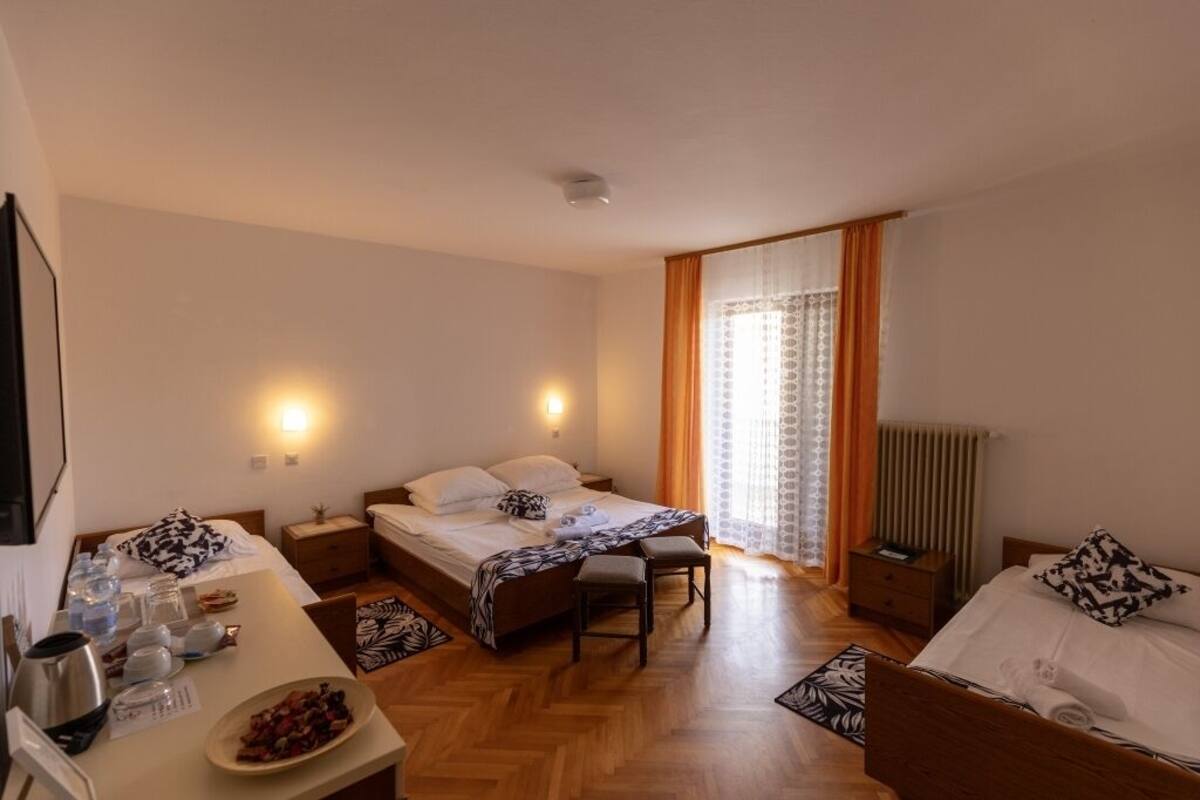 A hotel room with a bed, a desk, a chair, a radiator, and a window with curtains.