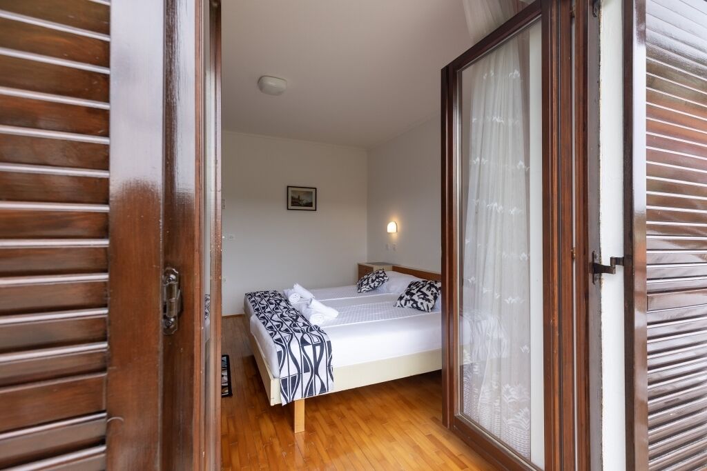 A bedroom with a bed, a bedside table, a nightstand, and a window with curtains.