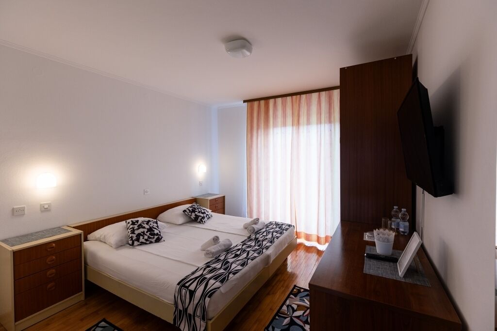 Habitación de hotel con cama, mesitas de noche, televisión de pantalla plana y ventana con cortinas.