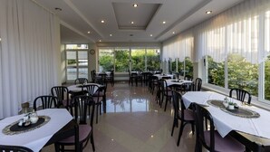 Un espace repas avec des tables et des chaises, de grandes fenêtres et une vue sur la verdure environnante.