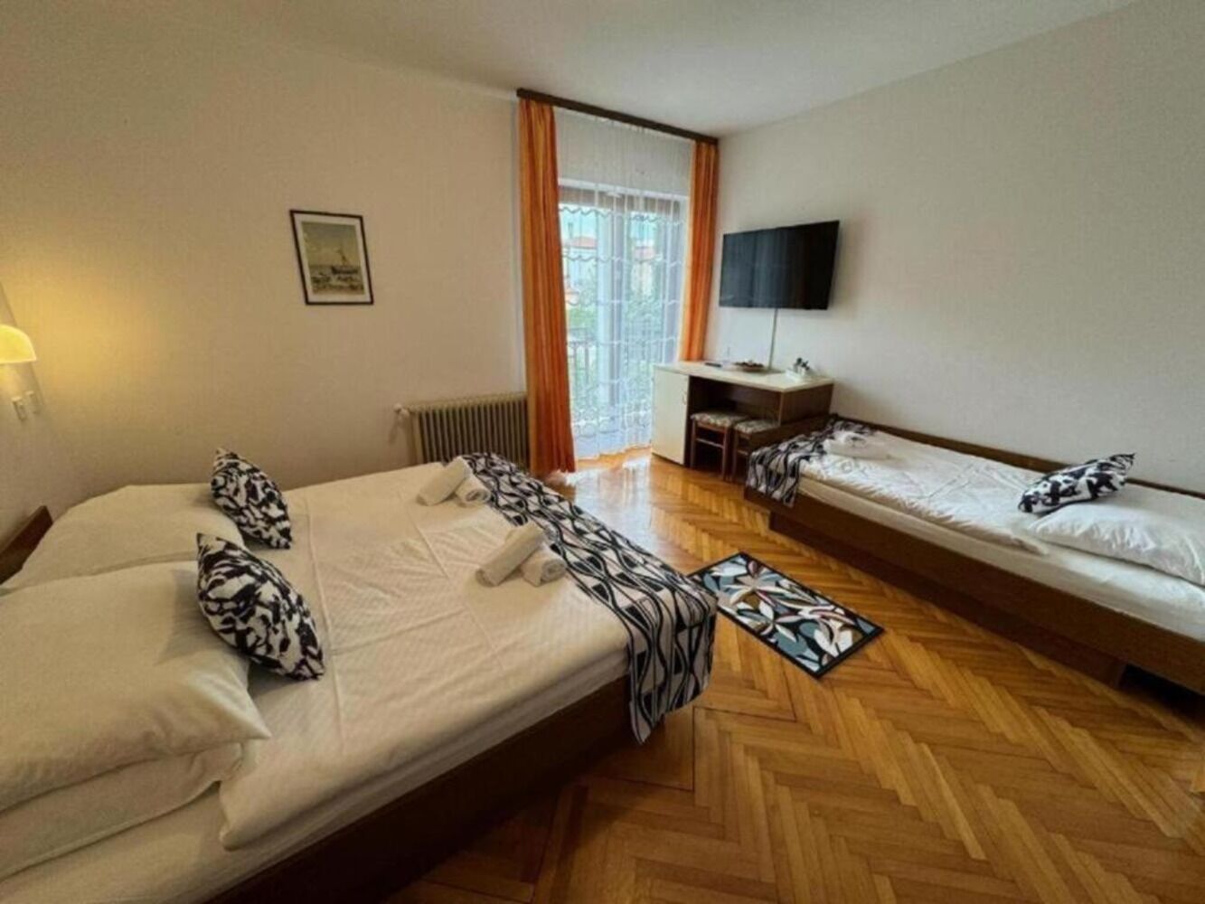 A hotel room with two beds, a desk, a chair, a TV, and a window with curtains.