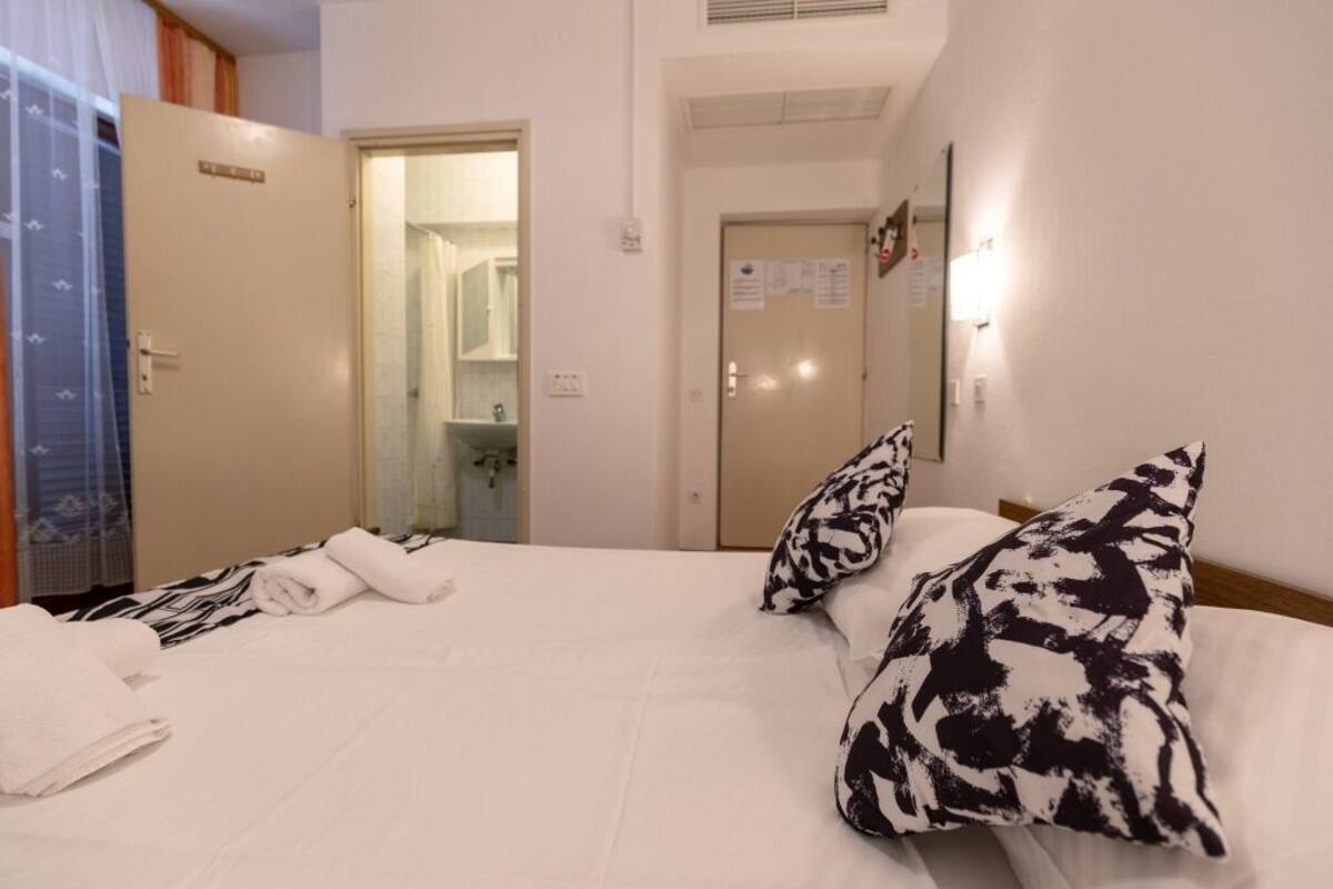 A hotel room with a bed, two pillows, a towel, a wardrobe, and a door leading to a bathroom.