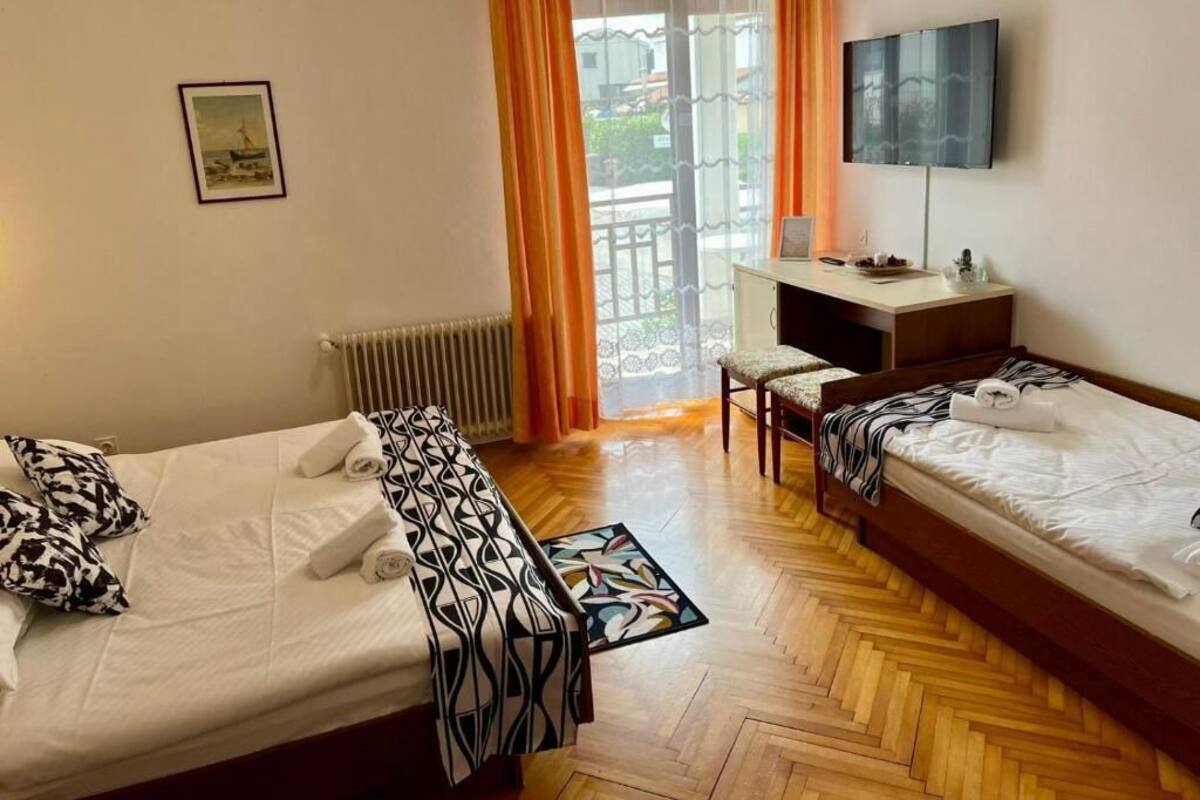 A hotel room with two beds, a desk, a chair, a TV, and a window with curtains.