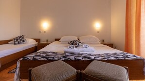 Une chambre d’hôtel avec deux lits simples, un grand lit et un canapé-lit. Il y a deux tables de chevet avec des lampes.