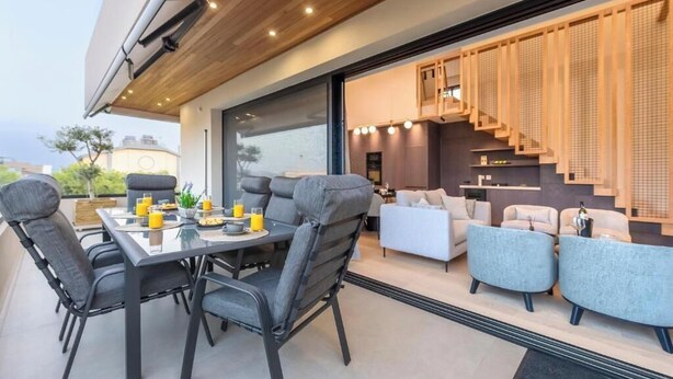 Et moderne udendørs spiseområde med et bord, stole, en sofa og en trappe til en etage over.