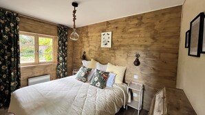 Een slaapkamer met houten lambrisering, een bed, nachtkastjes, een hanglamp en een raam met bloemen gordijnen.