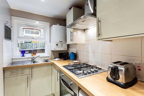 Kitchen area with gas stove, toaster, coffee maker, sink, and window.