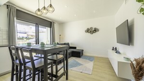Una sala de estar moderna con una mesa de comedor, sillas, un sofá y un televisor montado en la pared.