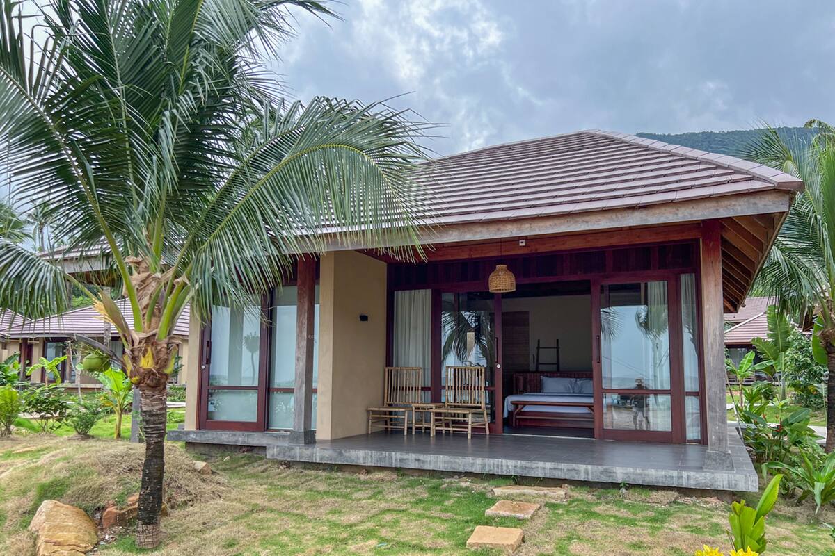 Ein Bungalow mit überdachter Veranda, großen Fenstern und Blick auf die umliegende Landschaft.