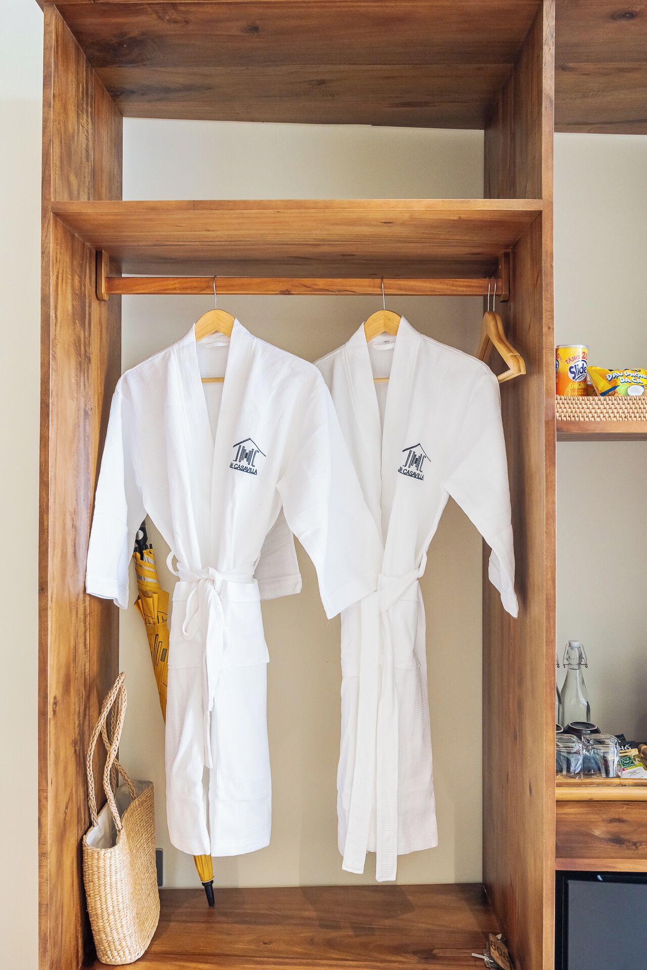 Two white robes hanging in a wooden frame, a woven basket, and a shelf with items.