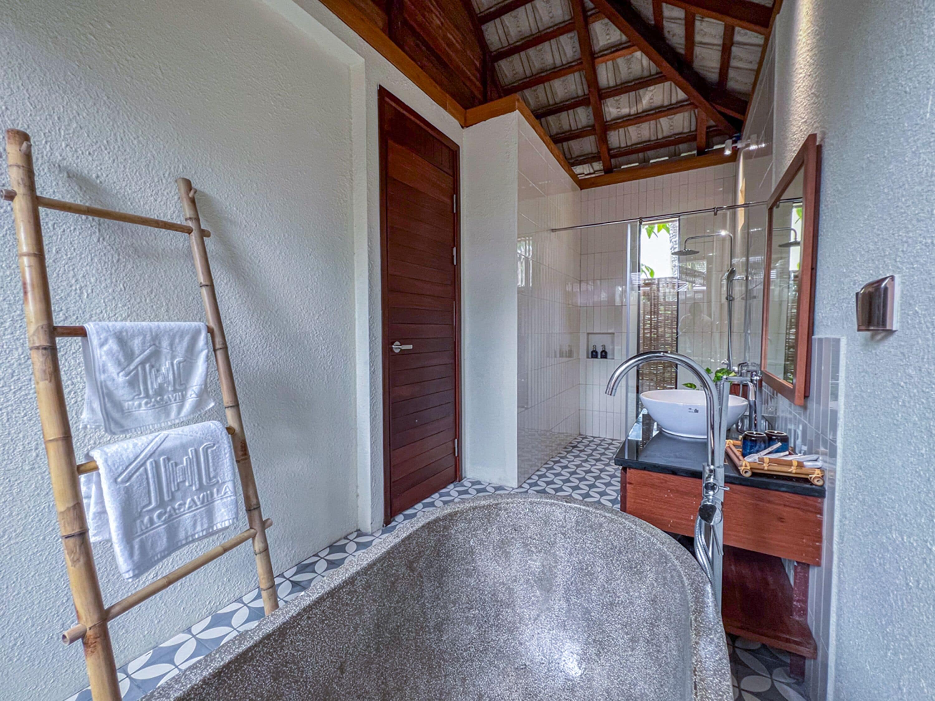 A bathroom with a large bathtub, a wooden ladder with towels, a wooden door, and a tiled floor.