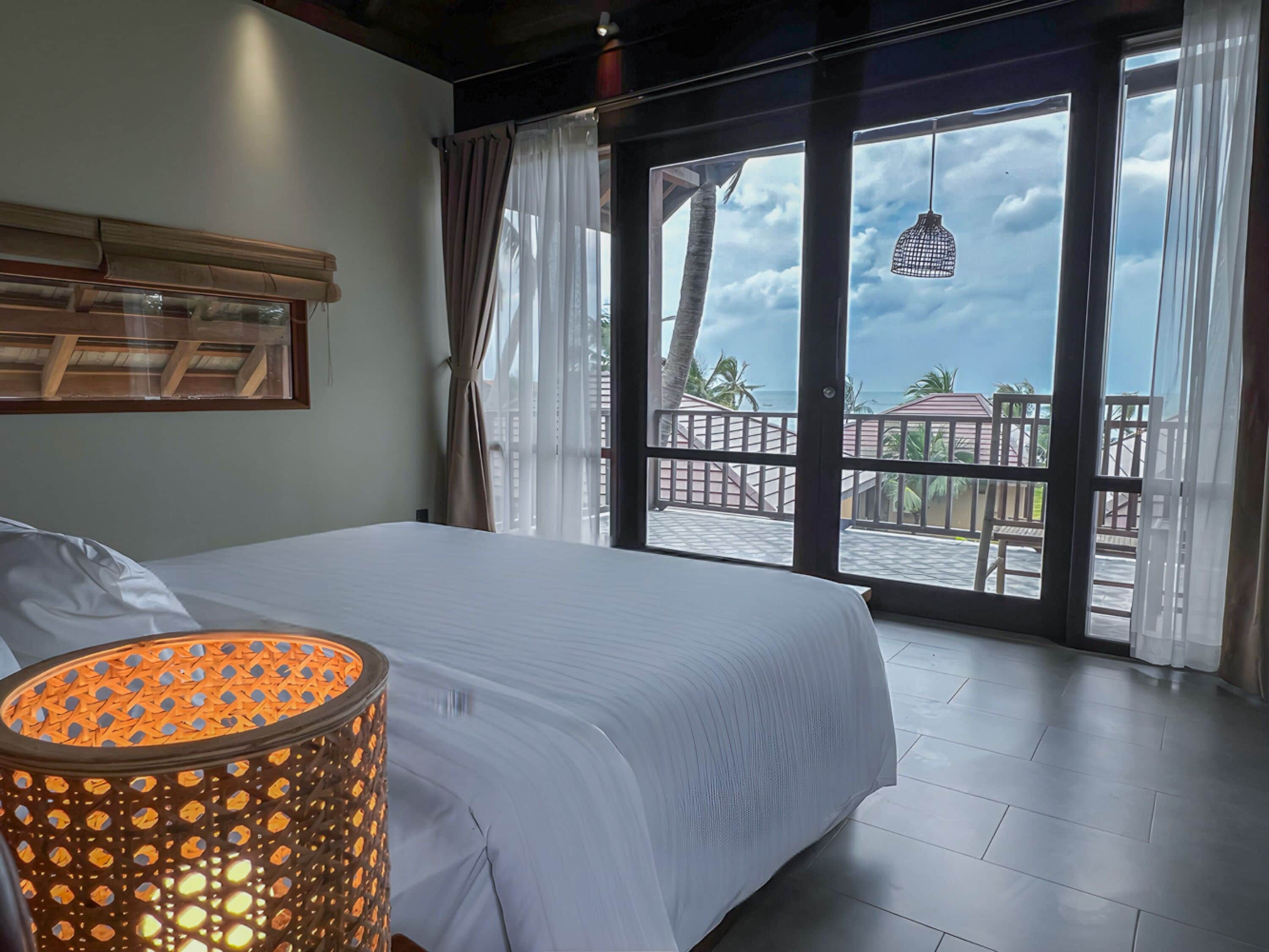 A bedroom with a large bed, a view of the balcony, and a hanging light fixture.