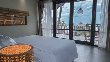 A bedroom with a large bed, a view of the balcony, and a hanging light fixture.