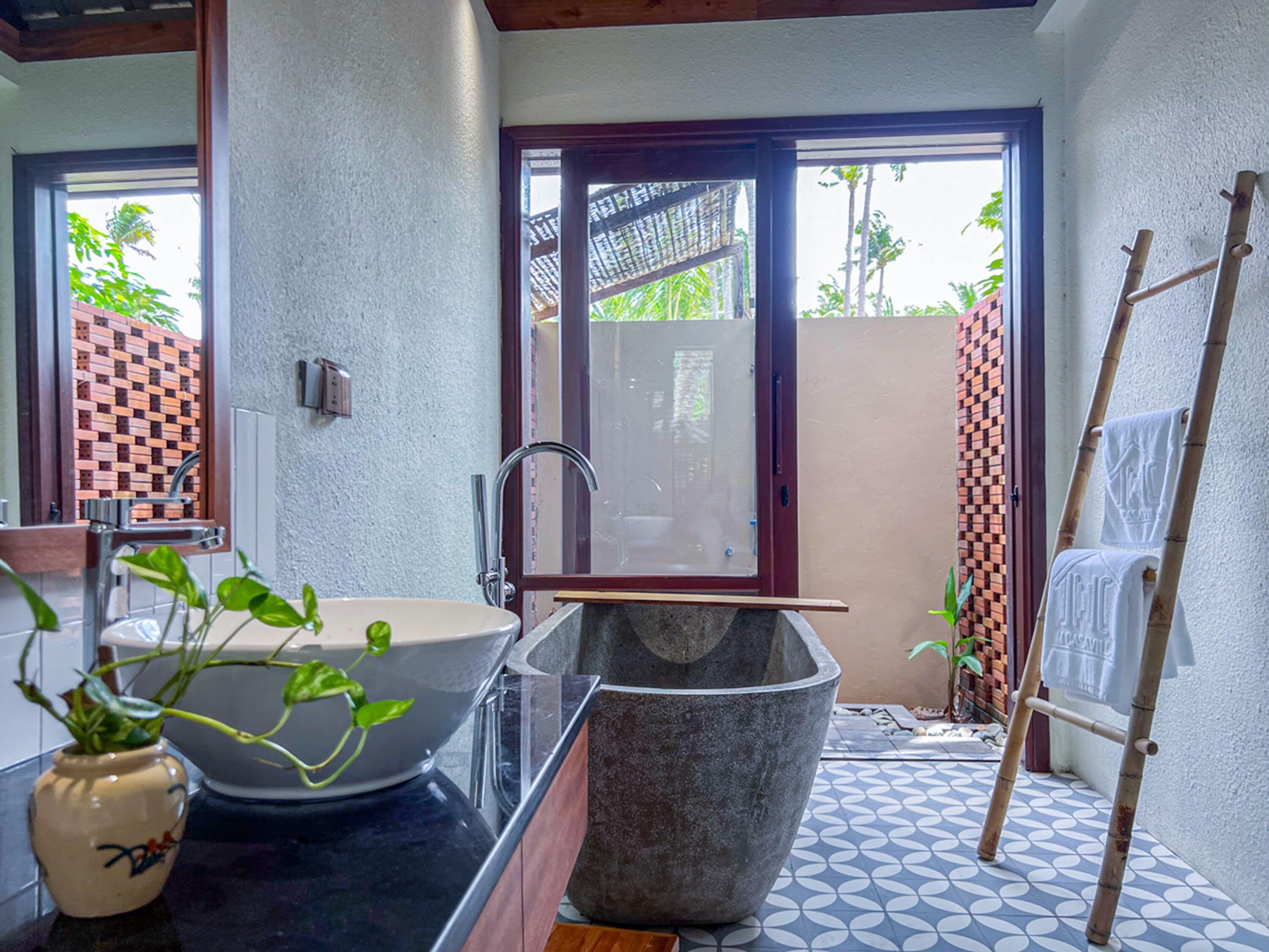 A bathroom with a large bathtub, a sink, and a shower area. There is a window with a view of greenery outside.