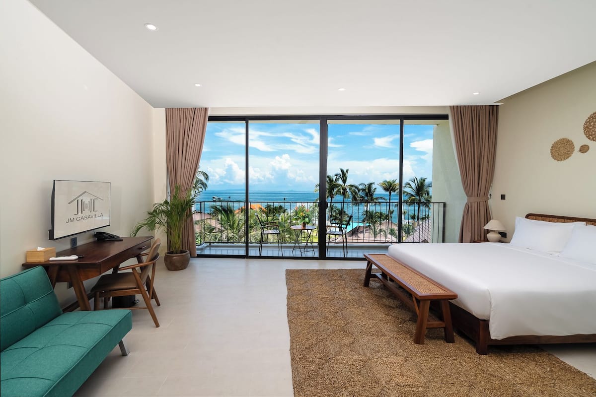 Ein Hotelzimmer mit großem Balkon, einem Bett, einem Schreibtisch mit Stuhl, einer Couch und einem Fernseher.