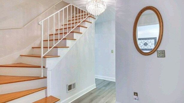 A staircase with wooden steps and white railings, a chandelier, and a mirror on the wall. - Masters Retreat! quite, great location 4BDR House (Augusta)