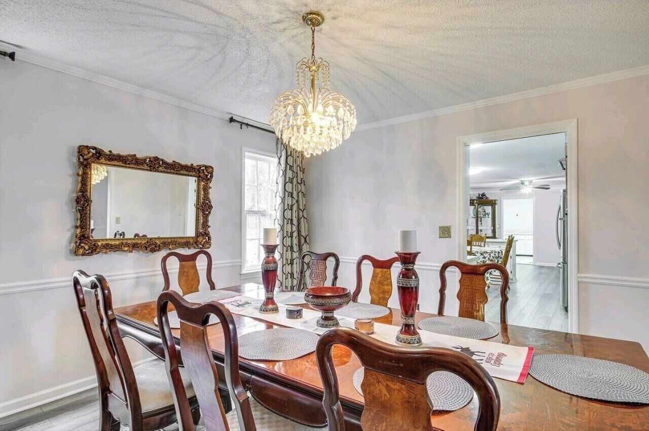 A dining room with a chandelier, ornate mirror, and wooden chairs.