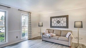 A living room with a beige sofa, two floor lamps, a decorative wall piece, and a window with a patterned curtain. - Masters Retreat! quite, great location 4BDR House (Augusta)