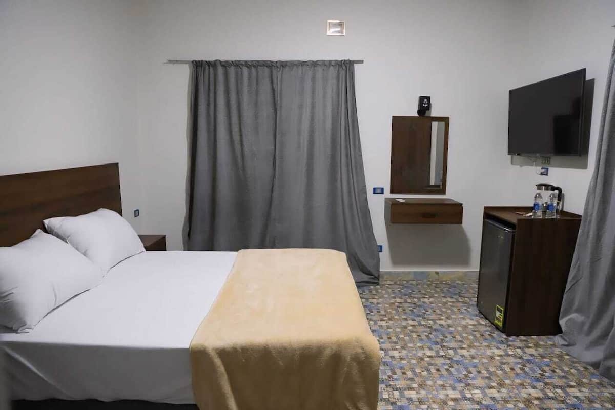 A hotel room with a bed, a desk, a television, and a small refrigerator.