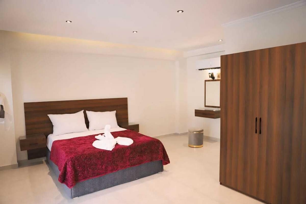 A modern hotel room with a large bed, wooden headboard, and a wardrobe.