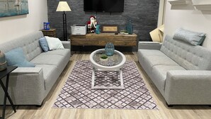 Un salon moderne avec deux canapés gris, une table basse, un téléviseur à écran plat et un mur décoratif.
