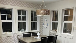 Un coin repas avec une table et des chaises en bois, un luminaire suspendu et un élément décoratif en forme d’ancre fixé au mur.