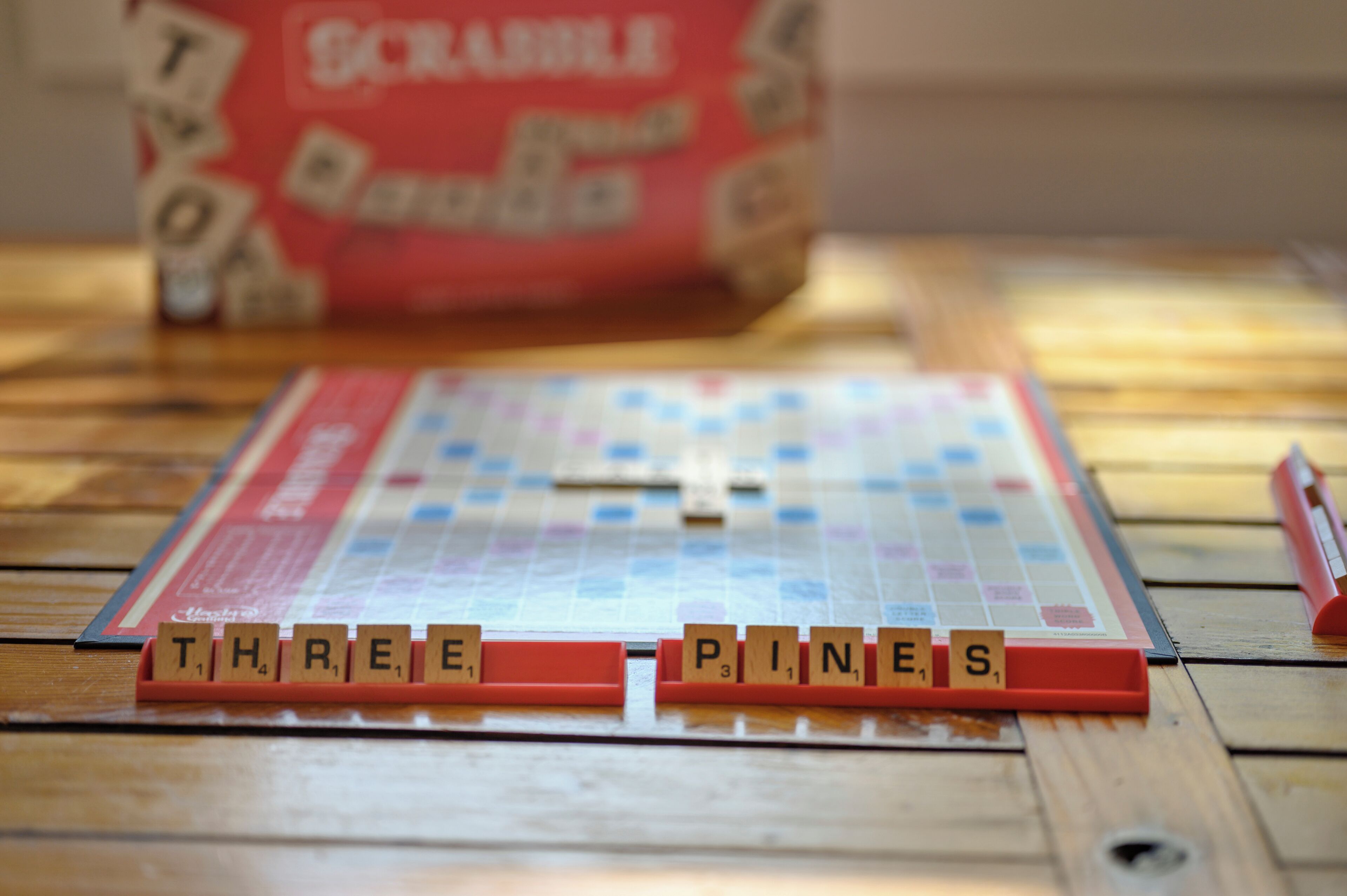 Ein Scrabble-Spielbrett mit Buchstabenkacheln, die die Wörter 'THREE PINE S' bilden, auf einem Holztisch.