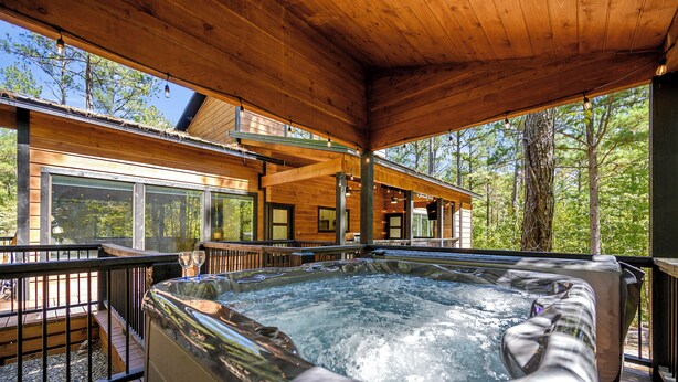 A hot tub on a wooden deck with a view of a cabin and trees.