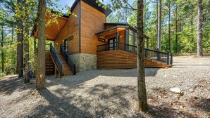 A wooden cabin with a stone foundation, surrounded by trees, featuring a staircase and a deck.