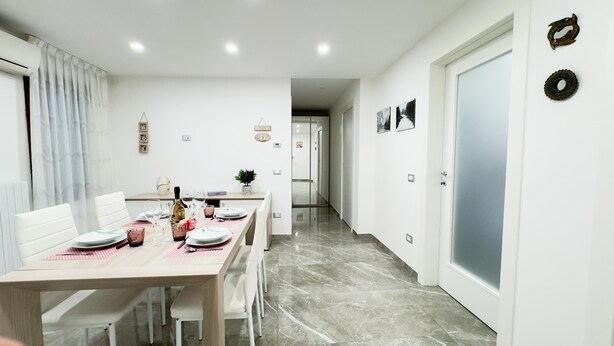 A modern dining area with a marble floor, white walls, and a wooden table set for four. - Casa Venturini by Ca-sa Check (Chioggia)