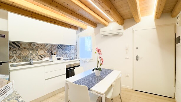 Una cucina moderna con mobili bianchi, una parete di fondo rivestita di piastrelle e un soffitto in legno.