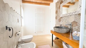 A bathroom with a hexagonal tile wall, a white toilet, a sink with a stone basin, and a wooden vanity. - Maison la Digue by Ca-sa Check (Chioggia)