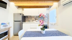 Una cucina compatta con mobili bianchi, un frigorifero in acciaio inossidabile e uno schienale piastrellato.