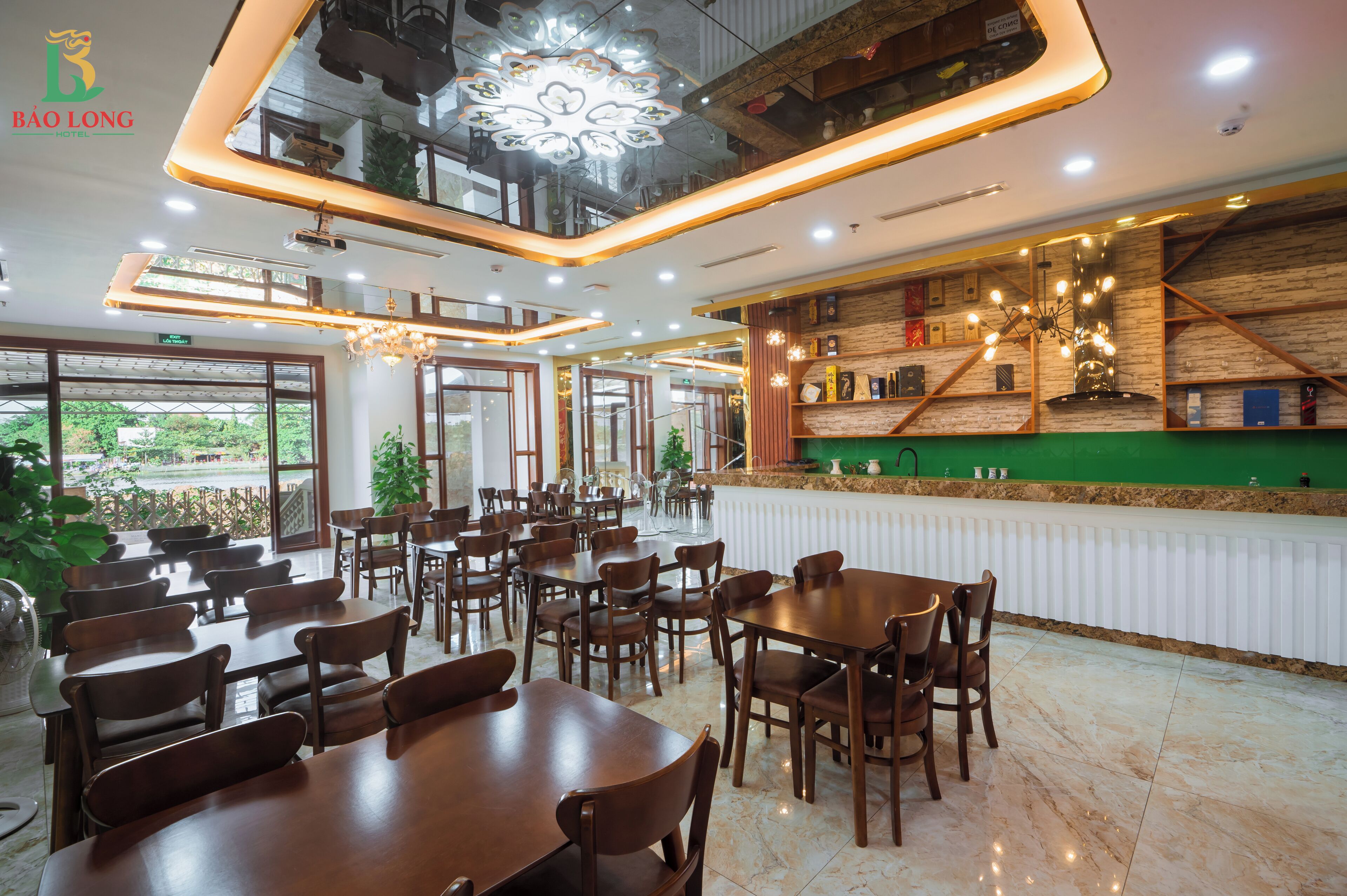A hotel dining area with multiple tables and chairs, a reception desk, and a view of the outdoors.