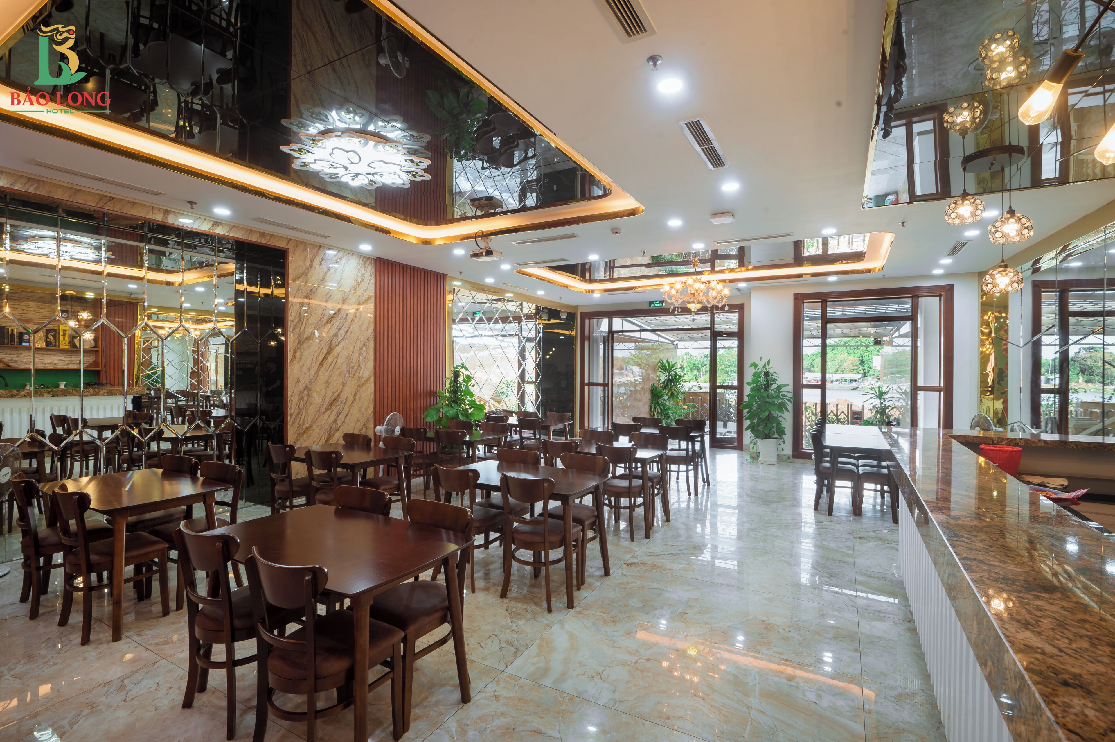 A spacious hotel dining area with multiple tables and chairs, a marble floor, and large windows allowing natural light.