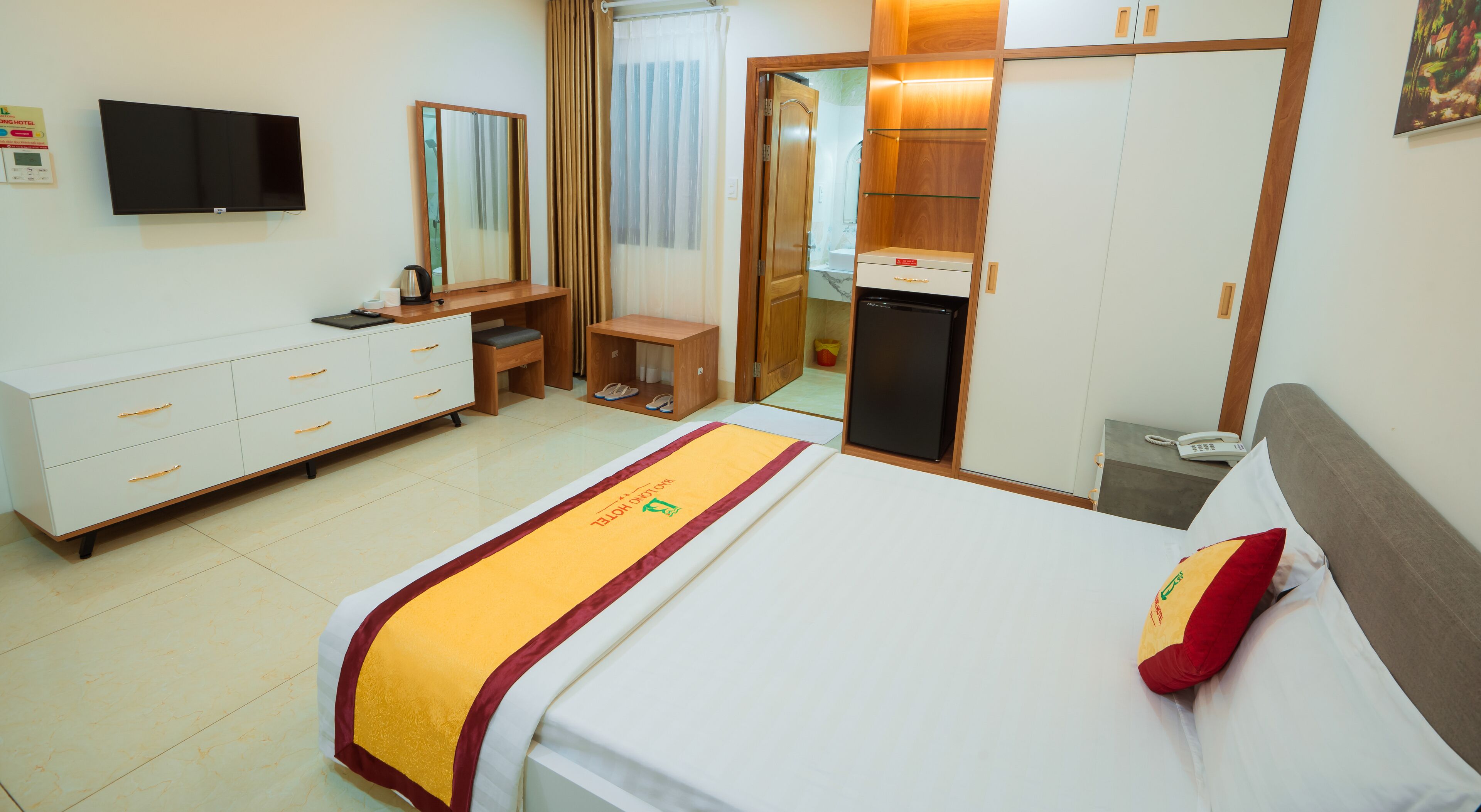 A hotel room with a bed, a desk, a wardrobe, a television, and a bathroom visible through an open door.